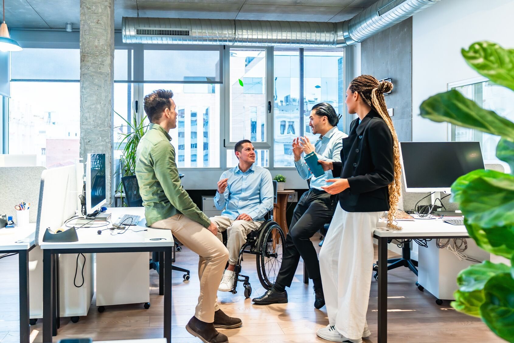 Web_Wide-Diverso equipo empresarial discutiendo un proyecto en una oficina moderna con un colega discapacitado en silla de ruedas